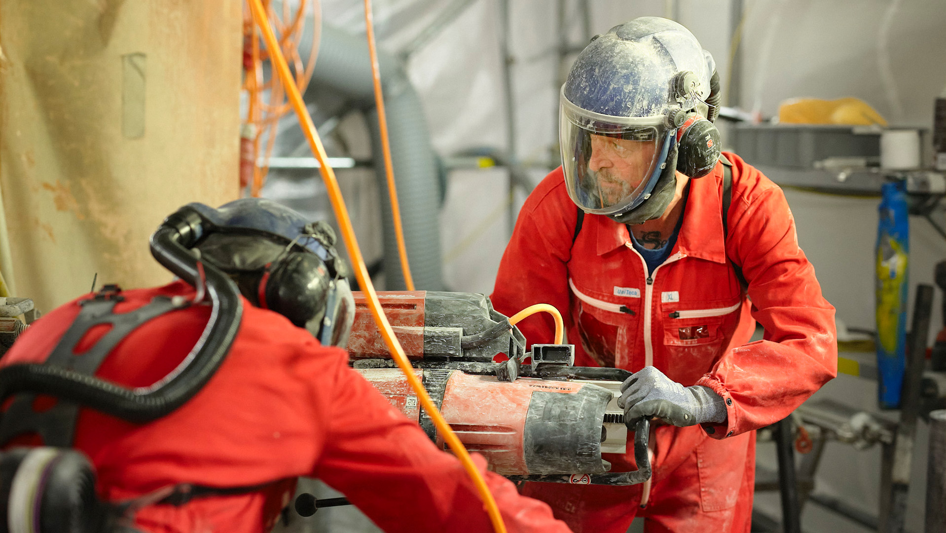 Zwei Männer in orangenen Arbeitsanzügen und Schutzhelmen